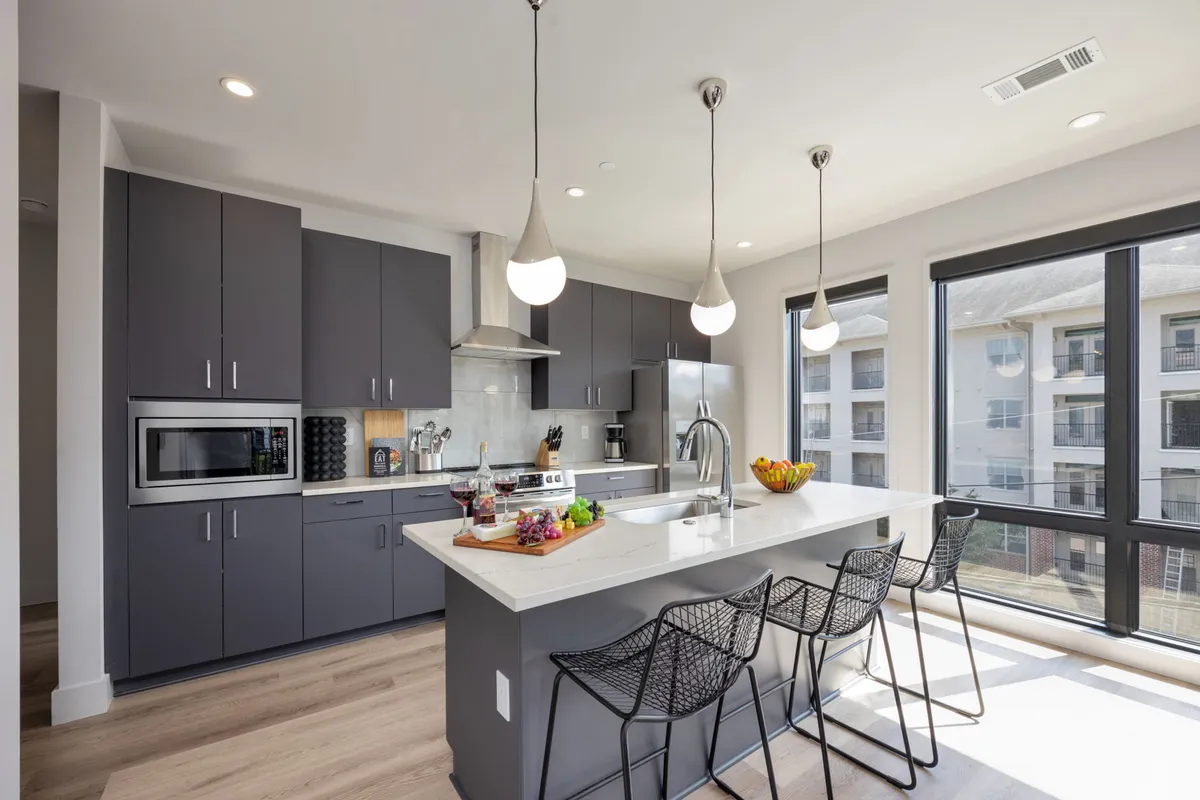 The photo focuses on an inviting kitchen with an island countertop adorned with snacks and drinks, large windows letting in ample natural light, and sleek cabinetry. The space is set up for entertaining, with a welcoming, stylish mood ideal for gatherings and chef-ready cooking.