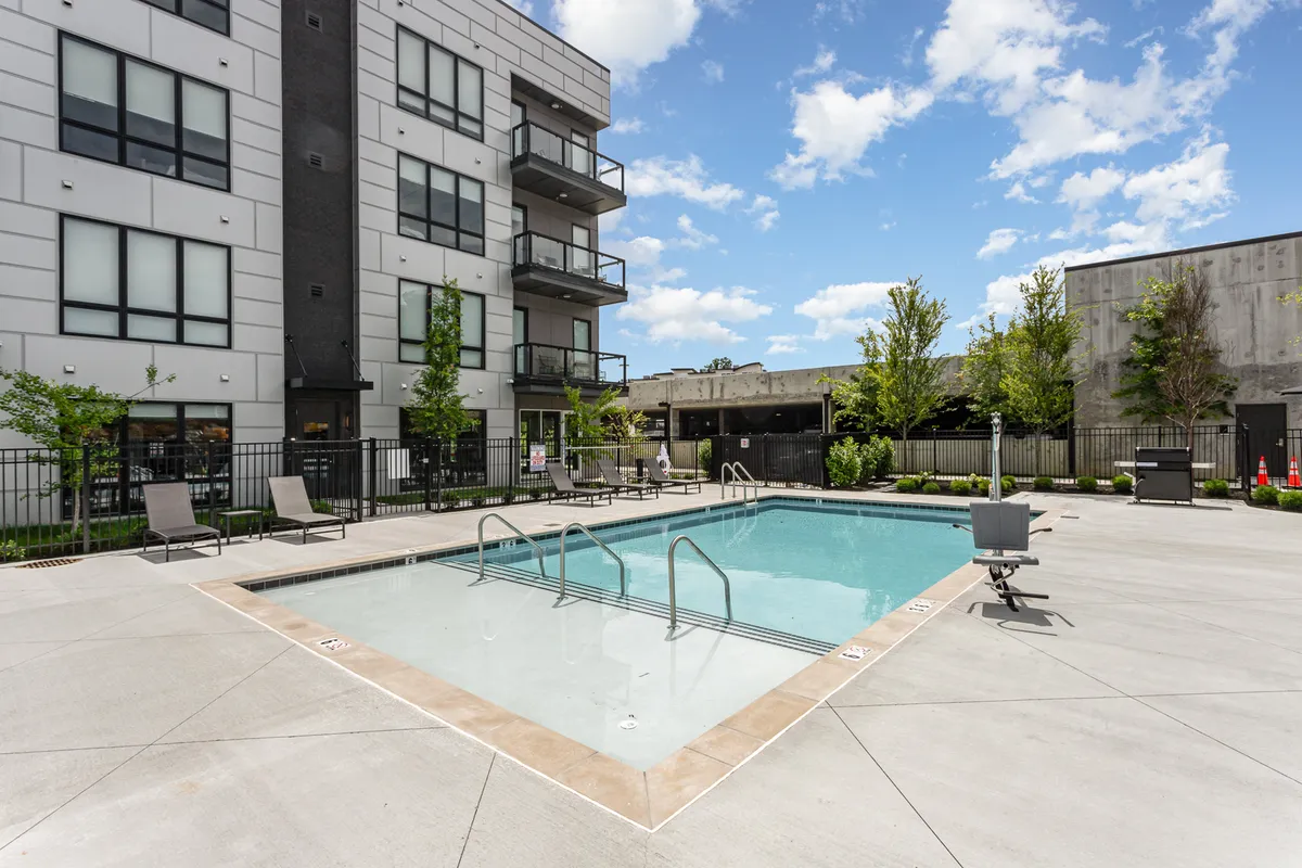 A modern swimming pool is the focal point, surrounded by lounge chairs and landscaped greenery, with balconies from the adjacent building overlooking the area. The image conveys a resort-style leisure atmosphere ideal for relaxing and socializing.