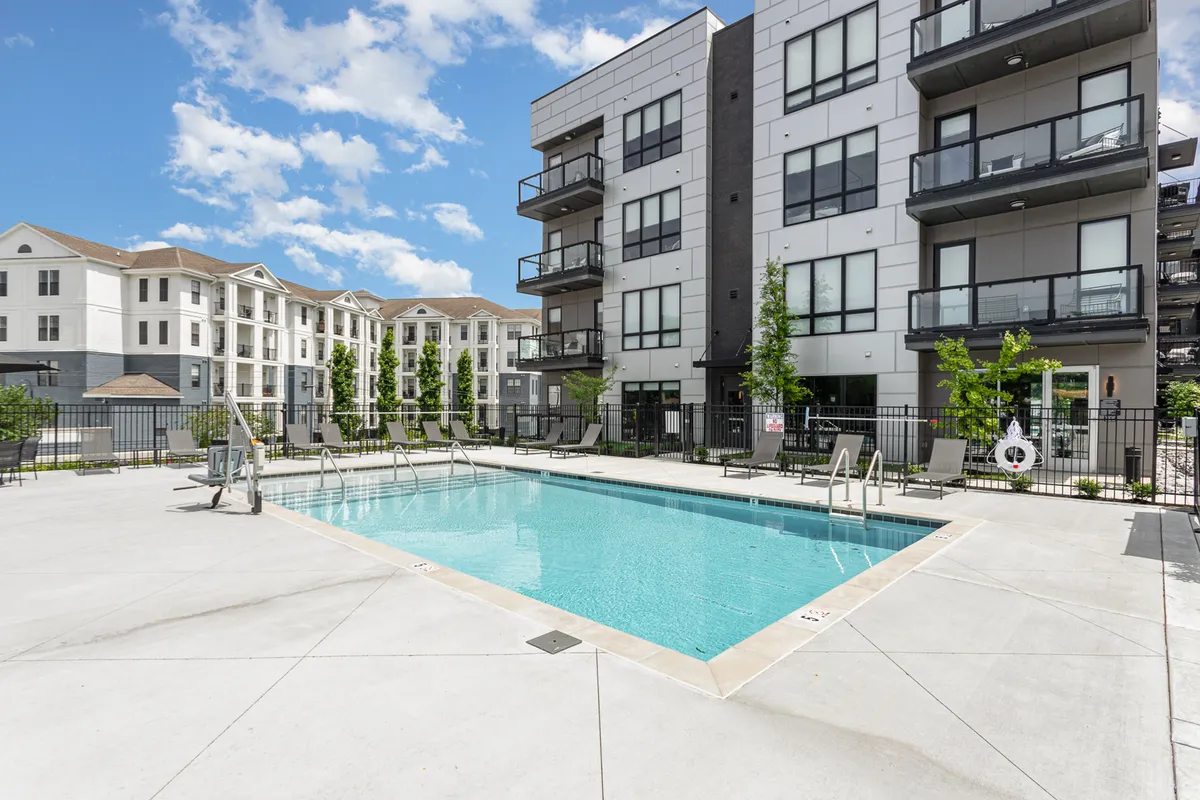A sparkling swimming pool set amidst modern apartment buildings and landscaped greenery. The scene is tranquil yet inviting, suggesting both the relaxation and social opportunities available to guests.