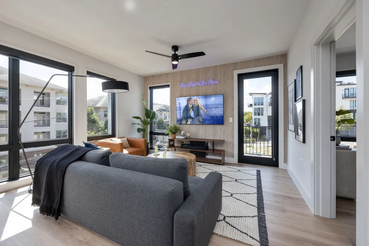 A comfortable and inviting living area featuring a sofa, television, large windows letting in natural light, and decorative plants. The space is designed for relaxation, socializing, and entertainment, embodying a sense of security and sanctuary above the urban bustle.