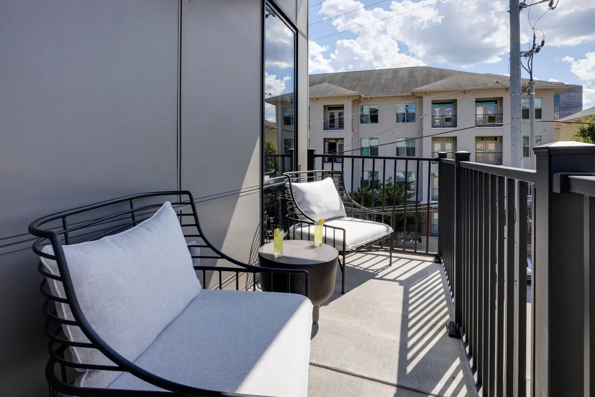 A serene balcony seating area with modern furniture, a small side table, and skyline views of the surrounding buildings, suggesting a peaceful oasis above the city bustle.