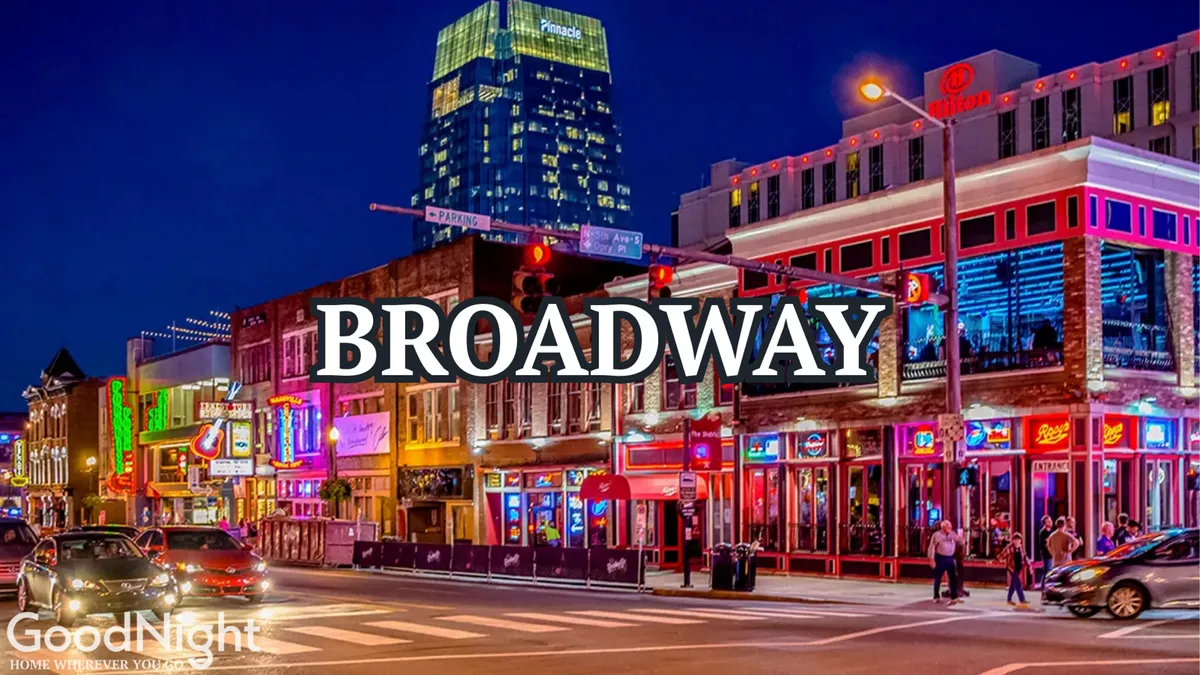 A vibrant city street illuminated by colorful neon signs, bustling with people out for dining, live music, and nightlife, all with the Nashville skyline in the background.